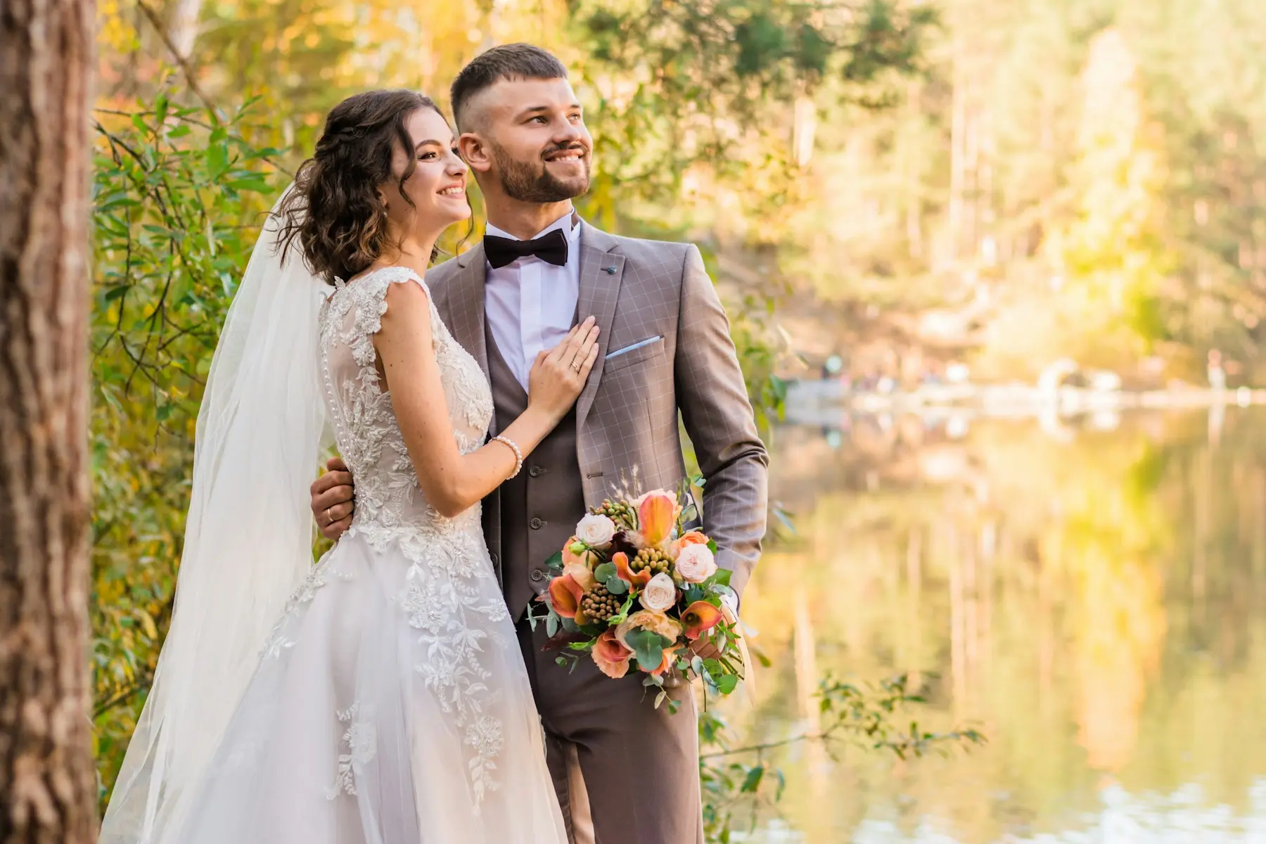 Newlyweds smiling beside an autumn lake